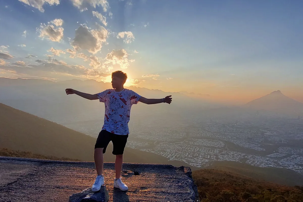Excursionista abre los brazos en la cima del Cerro de la Silla al atardecer sobre Monterrey