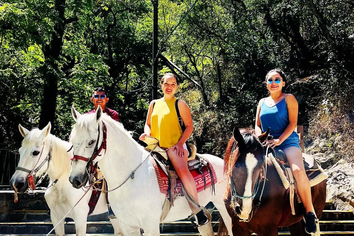 Turistas a caballo en el sendero hacia la cascada Cola de Caballo rodeados de bosque