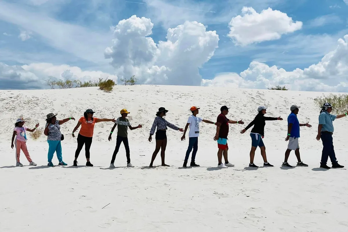 Grupo de viajeros camina tomado de la mano sobre las Dunas de Yeso de Cuatro Ciénegas al atardecer