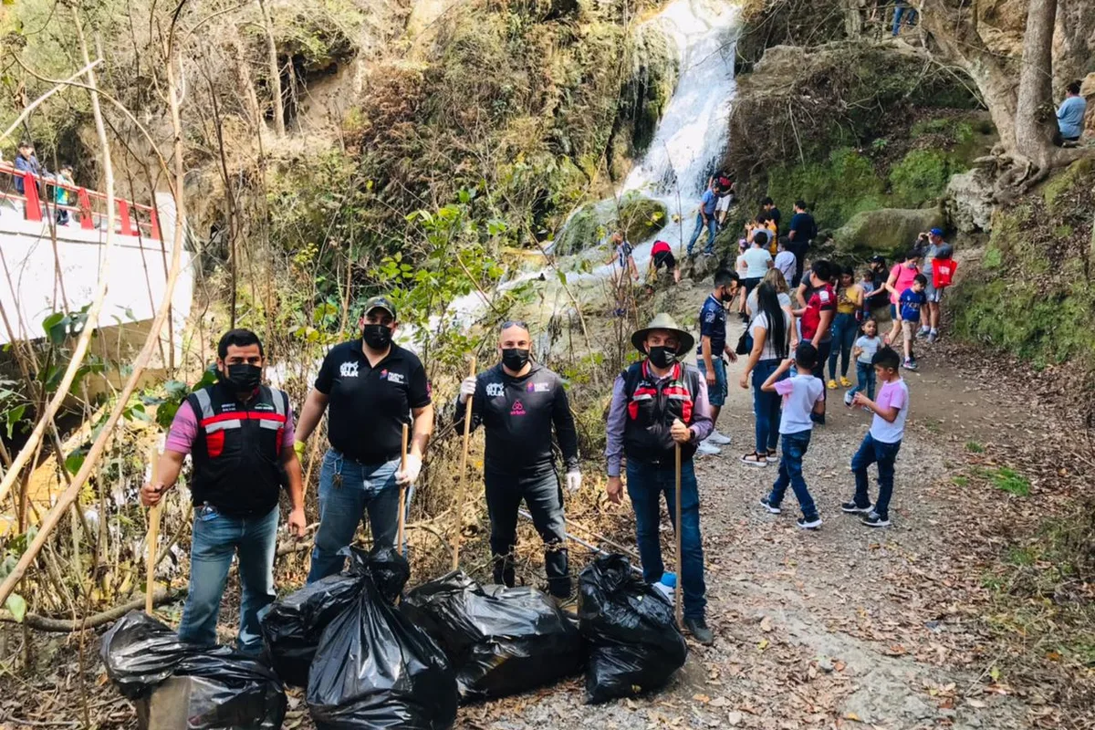 Equipo de Monterrey Tour recolectando bolsas de basura junto a una cascada durante campaña de limpieza ambiental