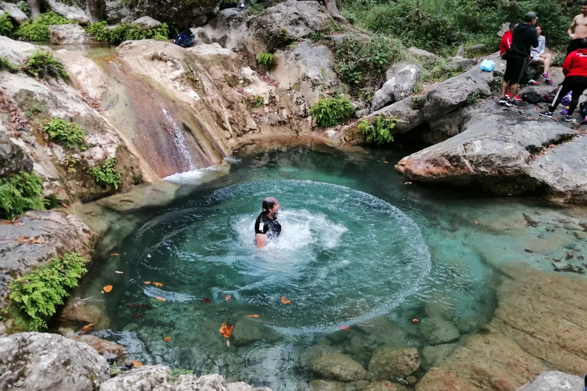 Nadador disfruta una poza circular de aguas turquesa junto a una pequeña cascada en La Estanzuela