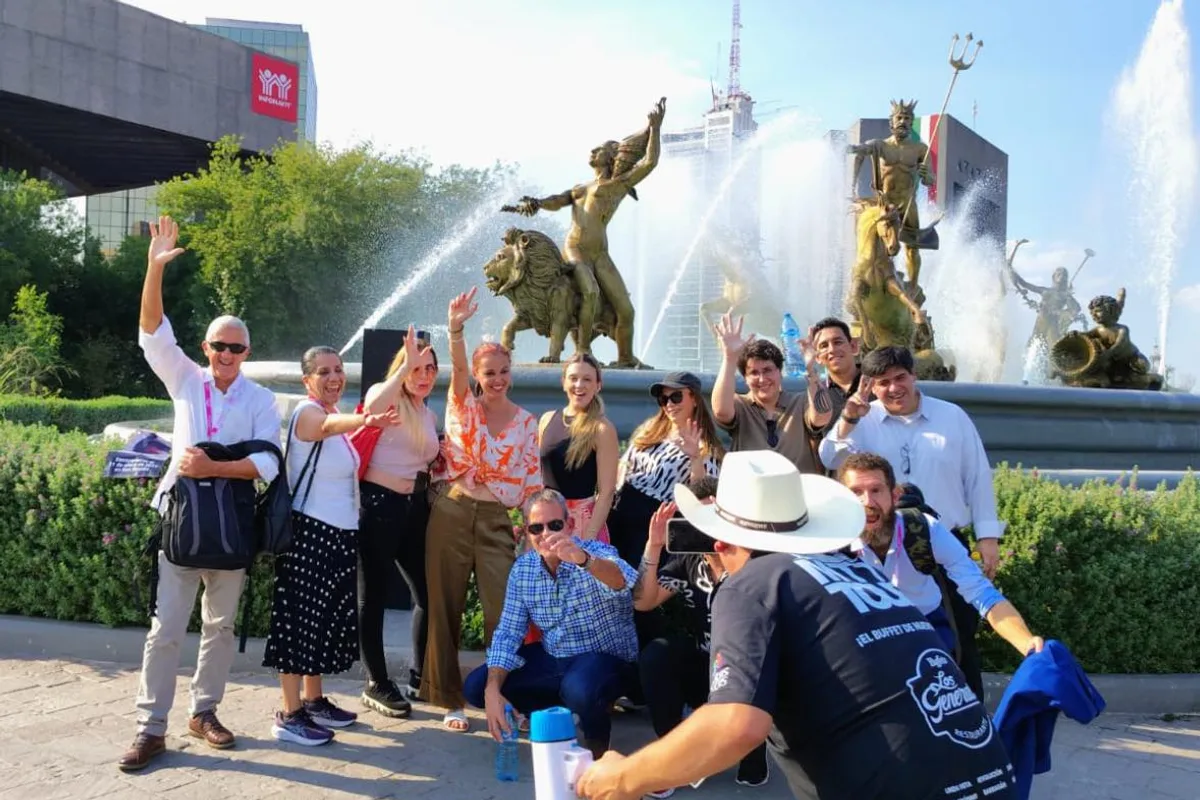 Grupo grande de turistas saluda frente a una fuente monumental durante un recorrido