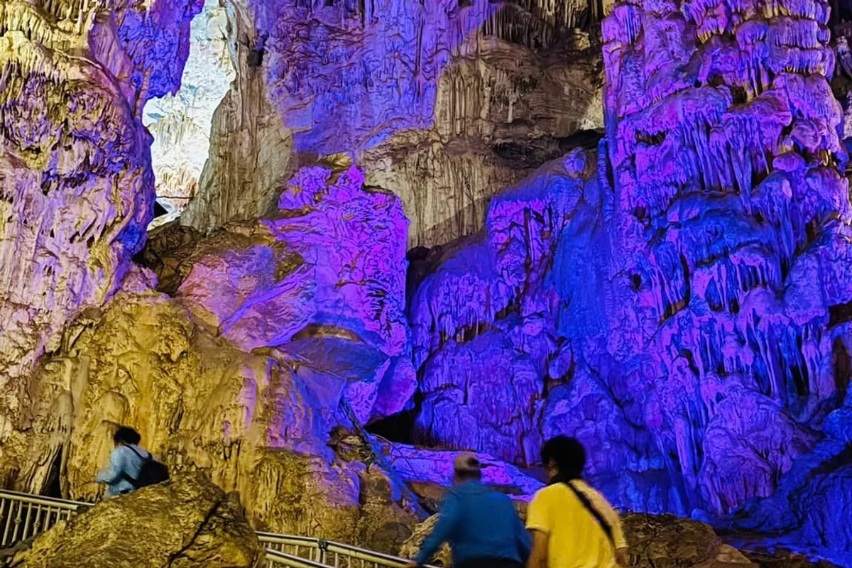 Salón interior de las Grutas de García iluminado en tonos azul y púrpura con visitantes