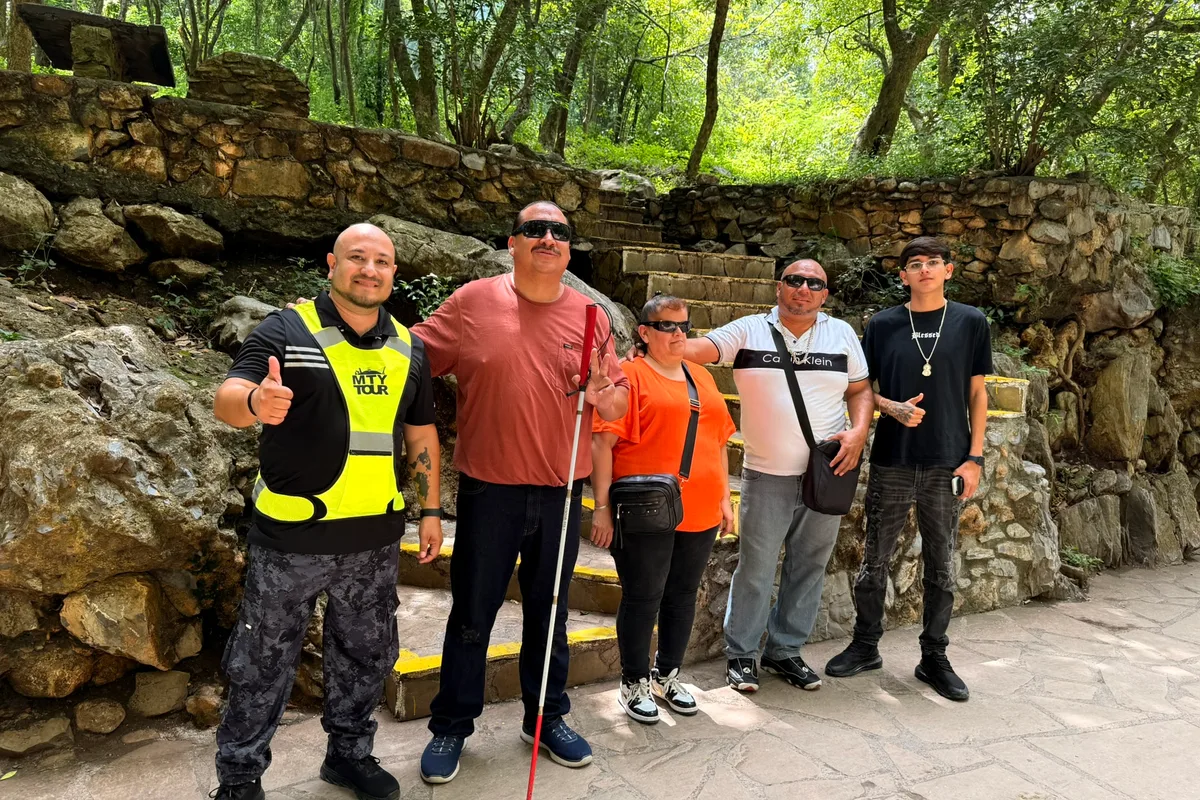 Grupo diverso de turistas incluye a una persona con bastón blanco frente a una cascada de Monterrey