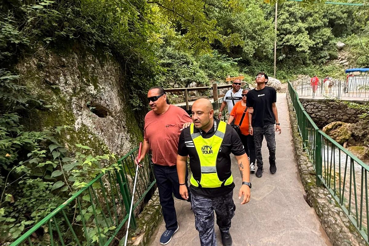 Guía turístico acompaña con cuidado a una persona con discapacidad visual y bastón blanco por un sendero
