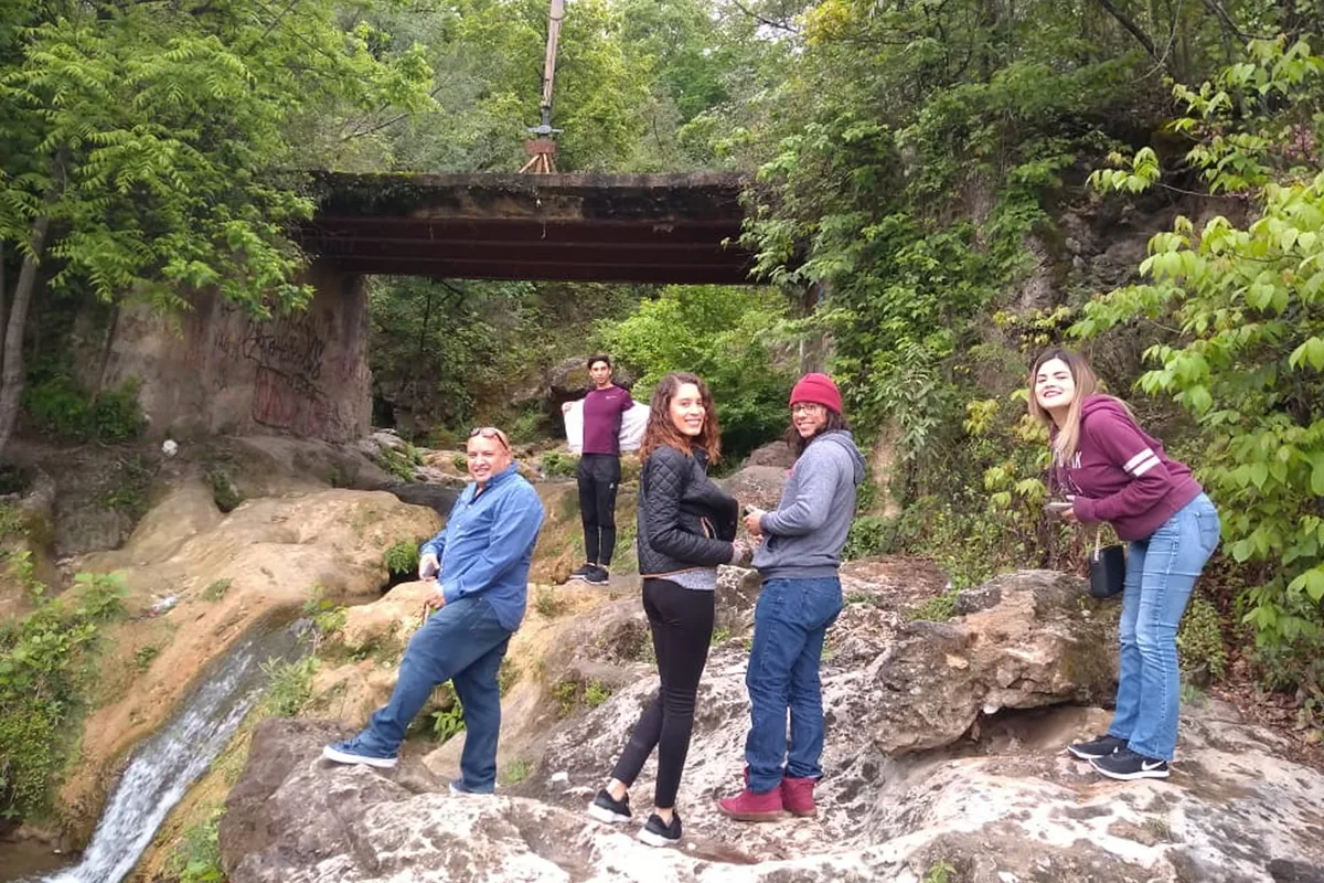 Grupo de amigos posa sobre rocas frente a cascada rodeada de vegetación en tour de aventura.