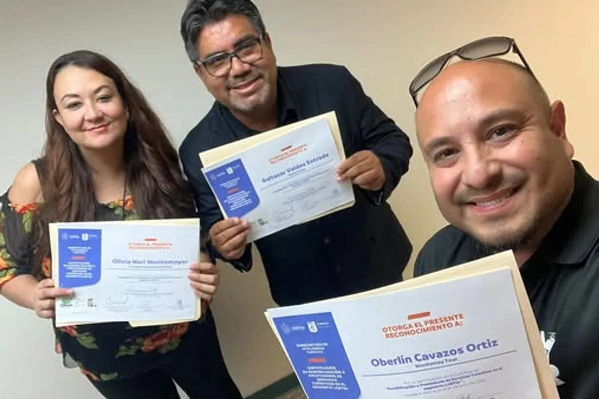 Tres profesionales del turismo sonríen mostrando sus reconocimientos oficiales de certificación en hospitalidad inclusiva.