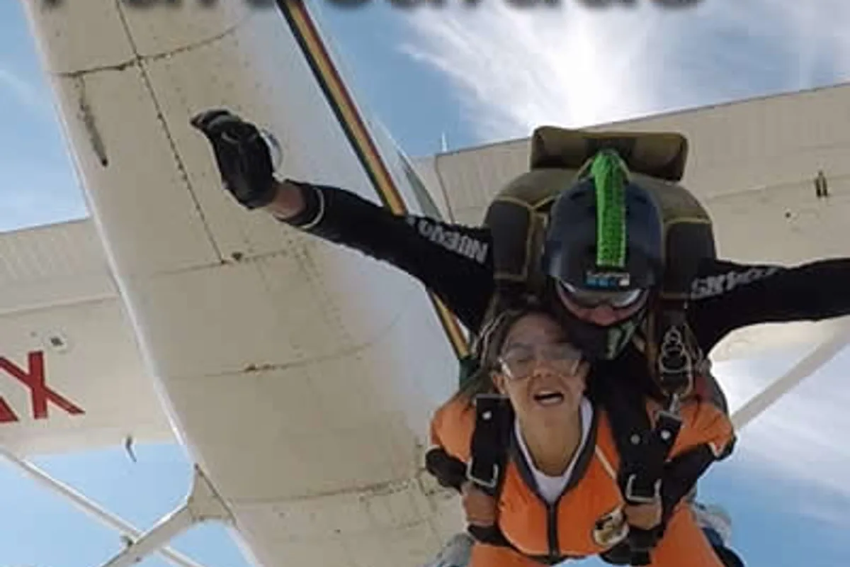 Turista sonríe con los brazos extendidos durante un salto en paracaídas junto a instructor certificado.
