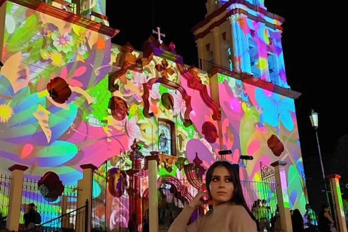 Fachada de la parroquia colonial iluminada con proyección de luces multicolor durante el festival nocturno