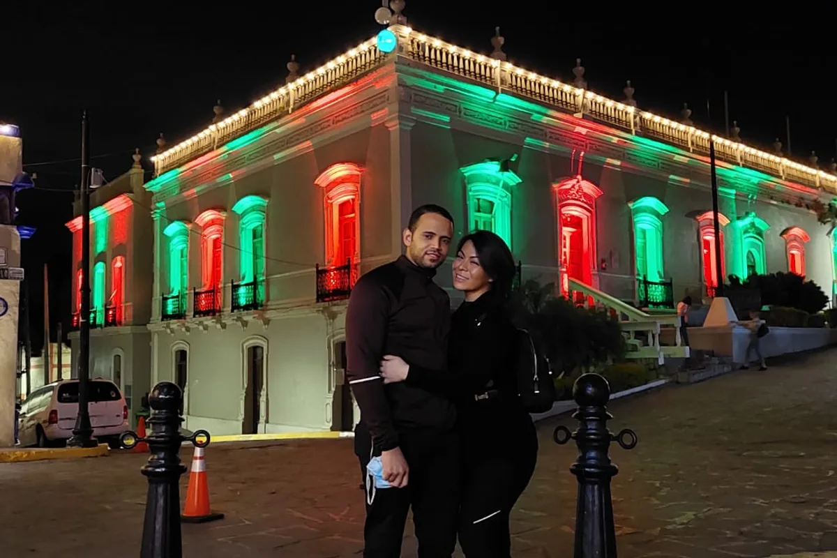 Pareja frente al edificio histórico del pueblo iluminado en verde y rojo durante la noche