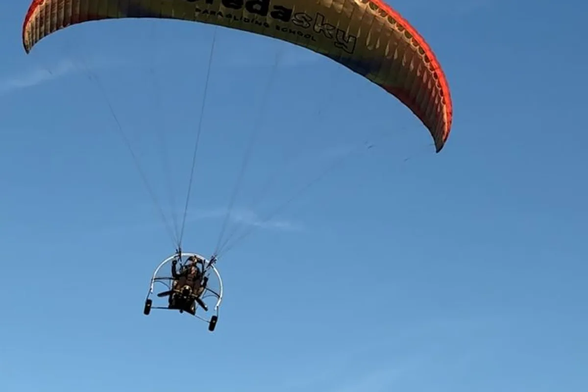 Vela de paratrike color naranja se recorta contra el cielo y la montaña
