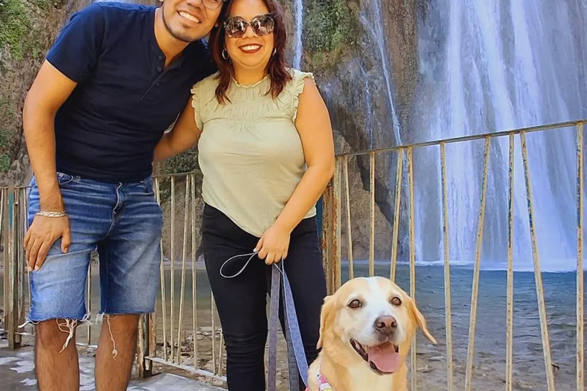 Pareja sonriente acompañada de su labrador disfruta la vista de una cascada en un recorrido incluyente