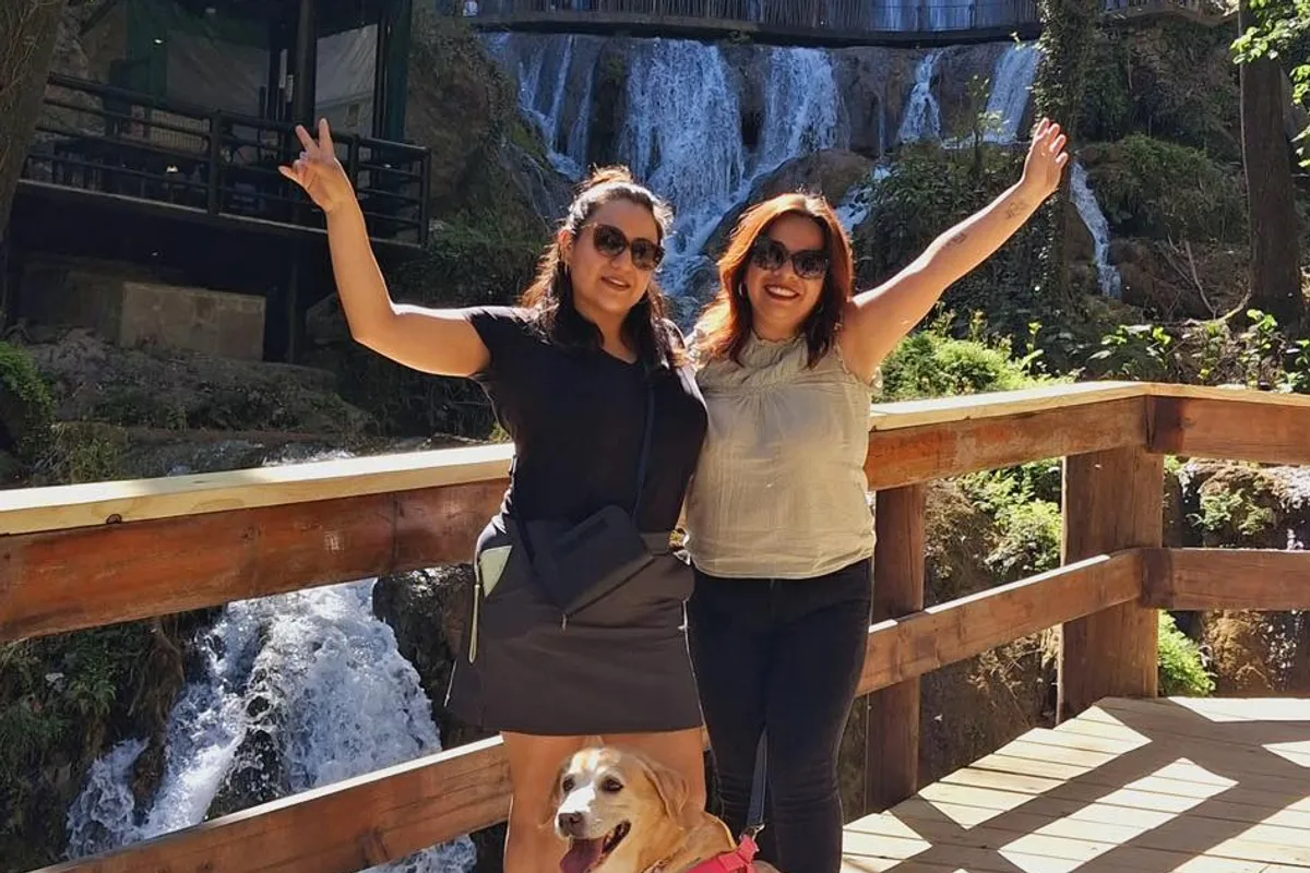Dos amigas celebran con los brazos en alto junto a su perro frente a una cascada en Monterrey