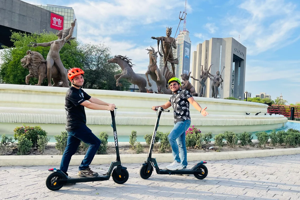 Dos turistas recorren en patín eléctrico la Fuente de Neptuno en la Macroplaza de Monterrey