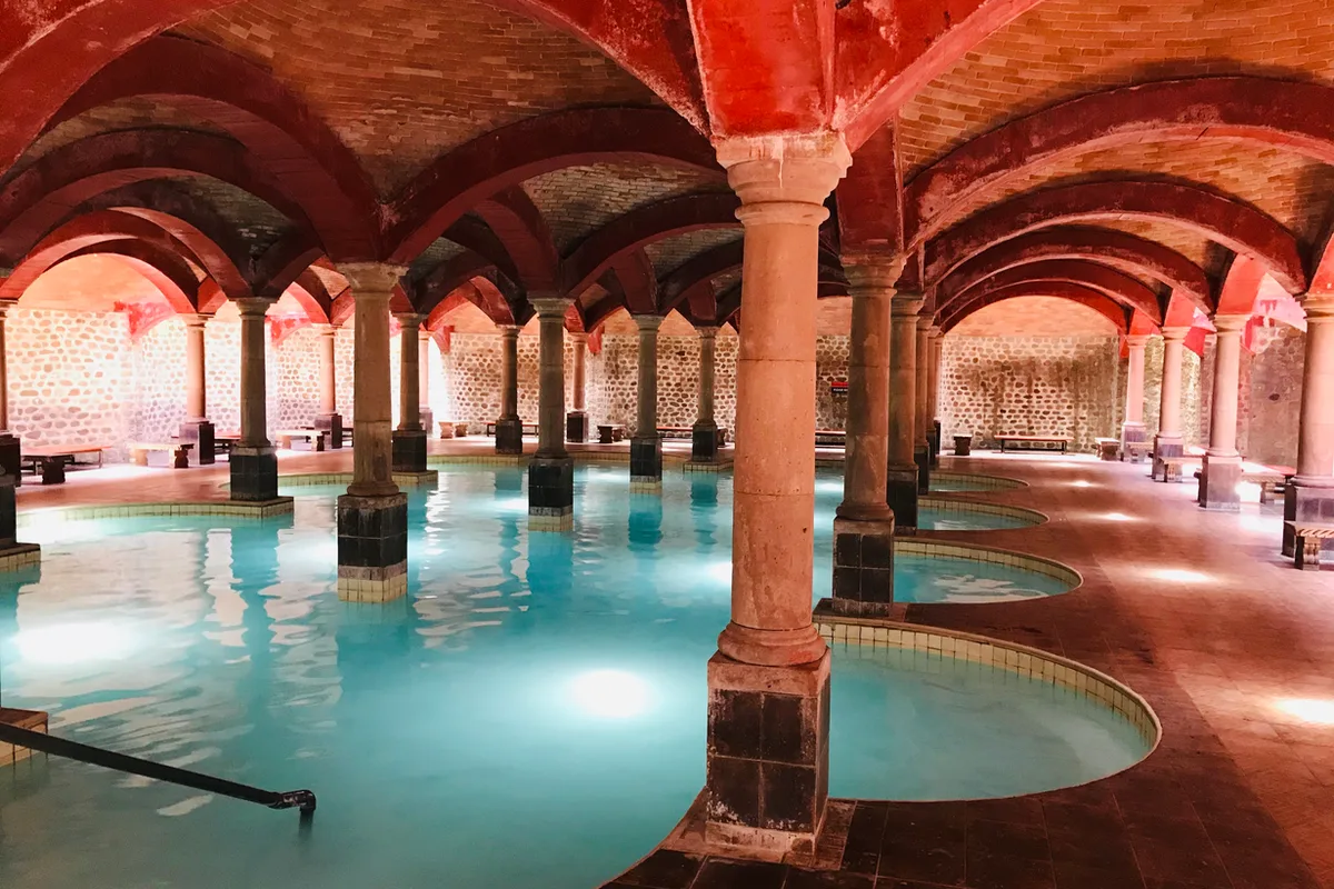 Salón de albercas termales bajo arcos de ladrillo rojo en las Termas de San Joaquín