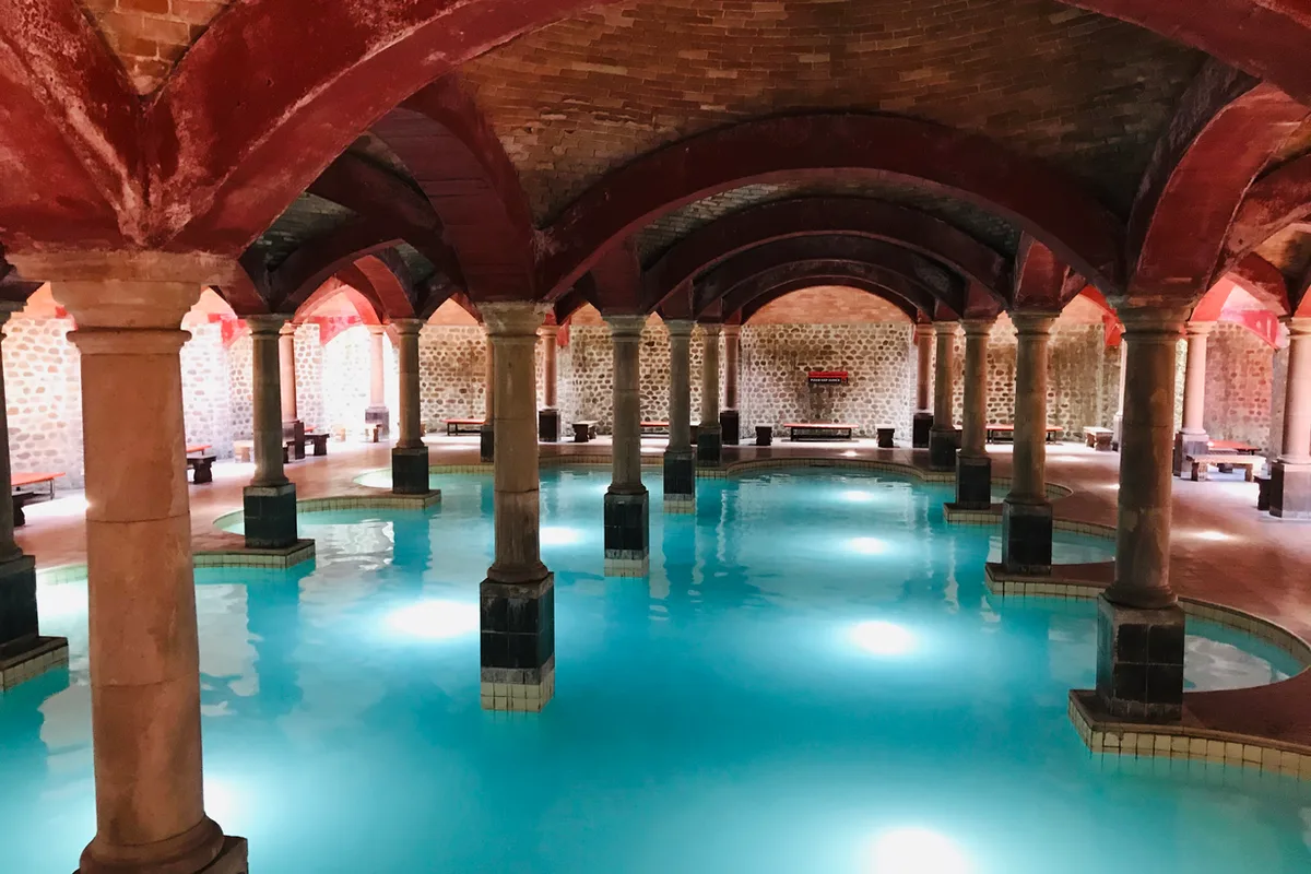 Amplia alberca techada con arcos de cantera y aguas termales cristalinas en Termas de San Joaquín