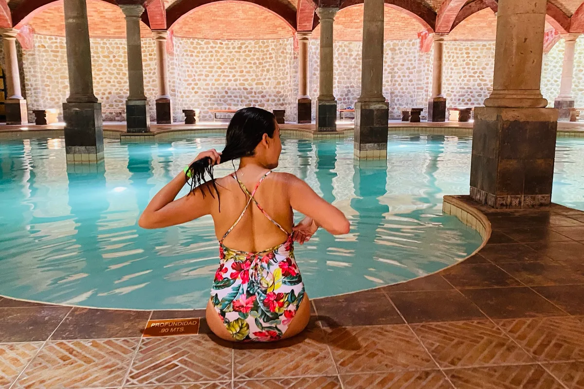 Mujer disfrutando del agua termal con los brazos abiertos bajo los arcos de piedra