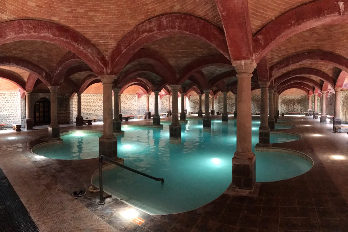 Alberca de aguas termales turquesa rodeada de arcos de ladrillo rojo en Termas de San Joaquín
